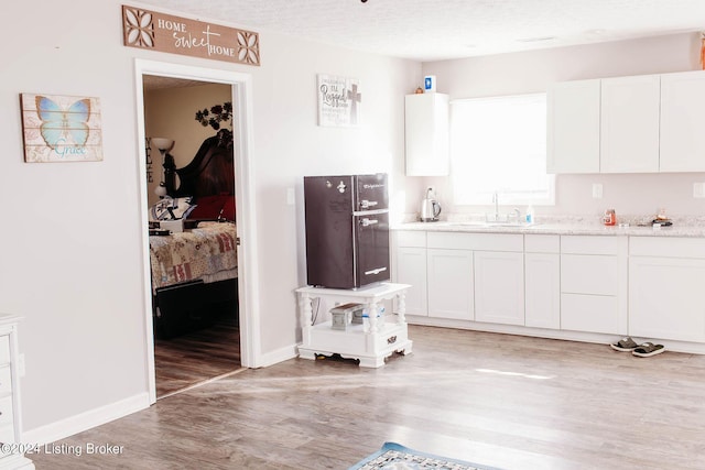 kitchen featuring white cabinets, light hardwood / wood-style floors, sink, and a textured ceiling