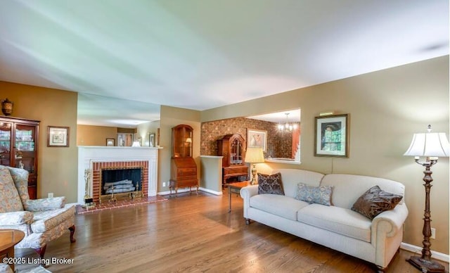 living room with a chandelier, wood-type flooring, and a brick fireplace