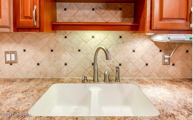 kitchen with backsplash, light stone countertops, and sink