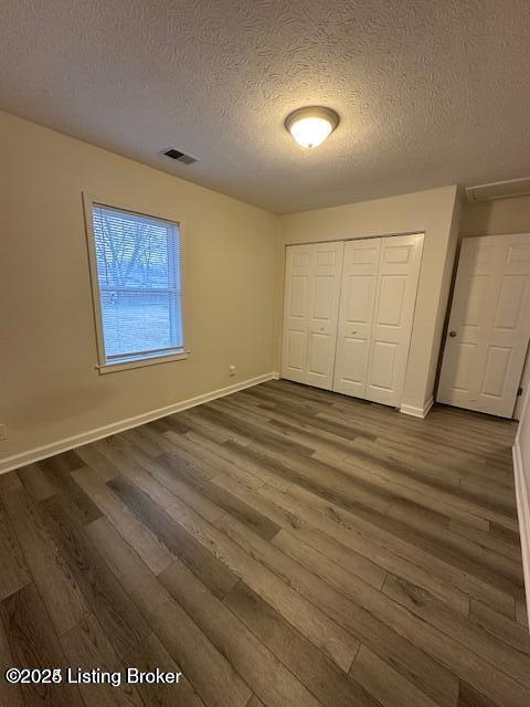 unfurnished bedroom with a textured ceiling, dark wood-type flooring, and a closet