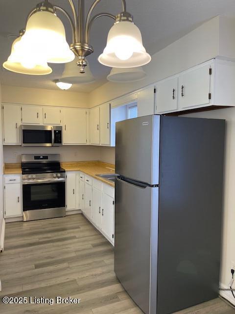 kitchen with white cabinets, stainless steel appliances, hanging light fixtures, and light hardwood / wood-style floors