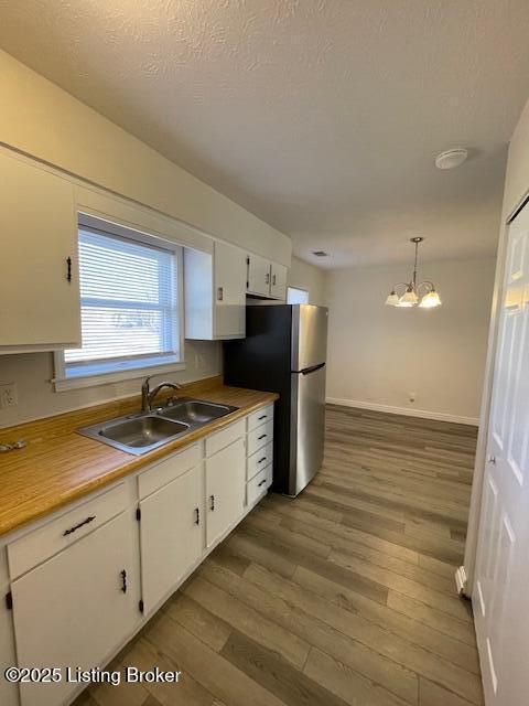 kitchen with stainless steel refrigerator, white cabinetry, sink, a chandelier, and pendant lighting