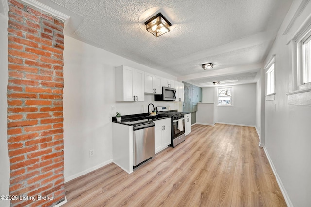 kitchen featuring sink, a textured ceiling, light wood-type flooring, stainless steel appliances, and white cabinets