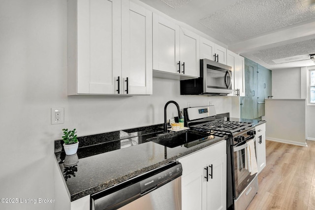 kitchen featuring sink, white cabinetry, a textured ceiling, appliances with stainless steel finishes, and dark stone counters