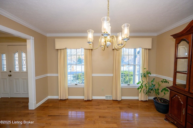 unfurnished dining area with a wealth of natural light, light wood-type flooring, crown molding, and an inviting chandelier