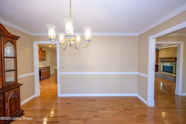 unfurnished dining area with a fireplace, an inviting chandelier, ornamental molding, and light hardwood / wood-style flooring