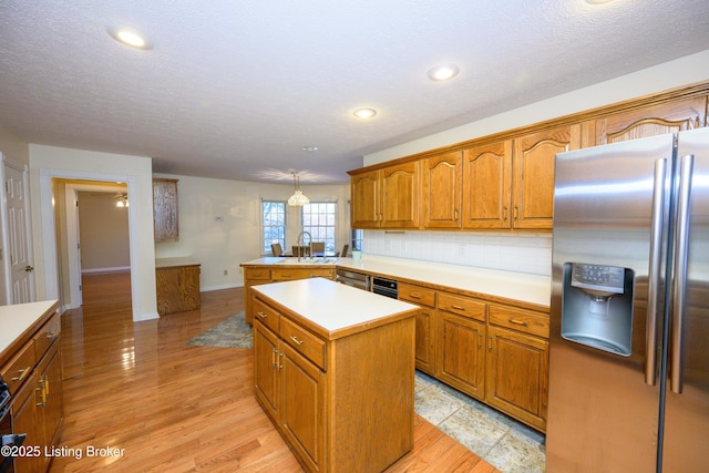 kitchen with pendant lighting, stainless steel refrigerator with ice dispenser, decorative backsplash, sink, and kitchen peninsula