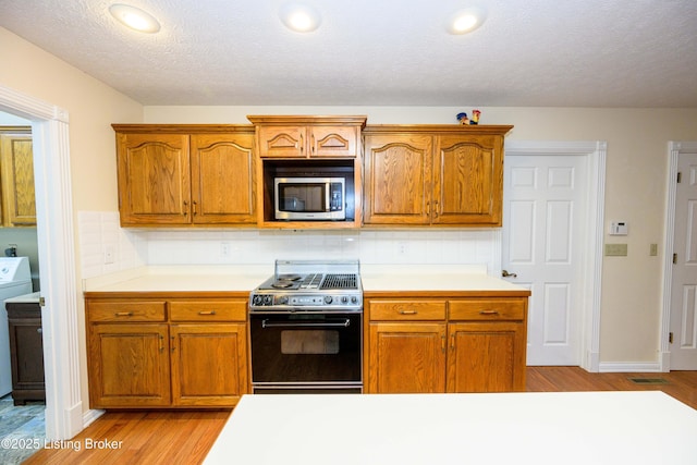 kitchen with backsplash, black electric range, washer / clothes dryer, light hardwood / wood-style flooring, and a textured ceiling