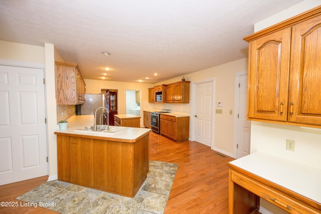 kitchen featuring light hardwood / wood-style floors, kitchen peninsula, sink, appliances with stainless steel finishes, and a textured ceiling