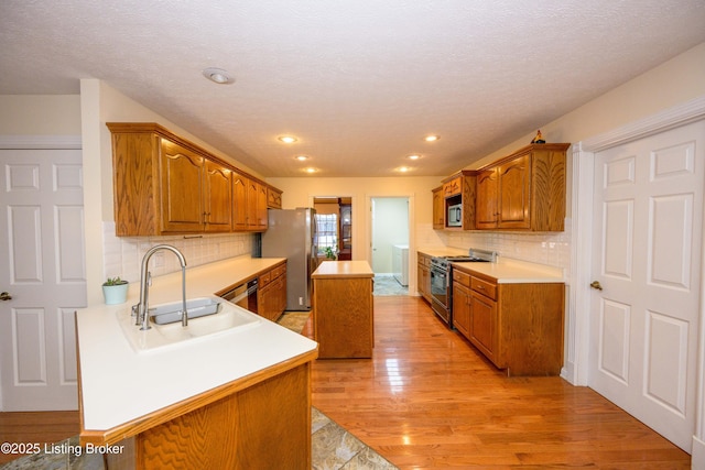 kitchen with appliances with stainless steel finishes, decorative backsplash, a kitchen island, light hardwood / wood-style flooring, and sink