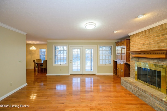 unfurnished living room with a fireplace, an inviting chandelier, light hardwood / wood-style flooring, a textured ceiling, and ornamental molding