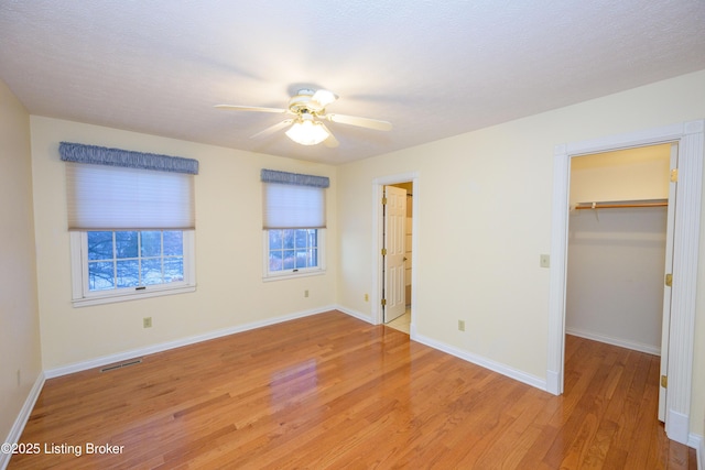 unfurnished bedroom with a textured ceiling, a walk in closet, a closet, ceiling fan, and light hardwood / wood-style flooring