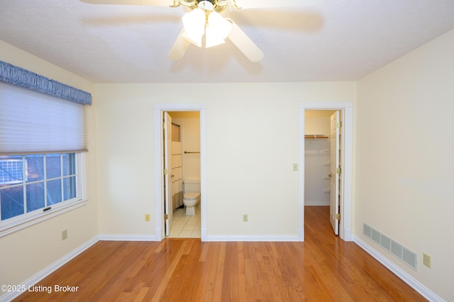 unfurnished bedroom with ceiling fan, light hardwood / wood-style floors, ensuite bath, a spacious closet, and a closet