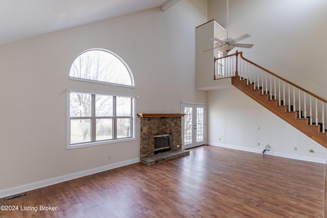 unfurnished living room with a stone fireplace, ceiling fan, dark hardwood / wood-style flooring, and a high ceiling