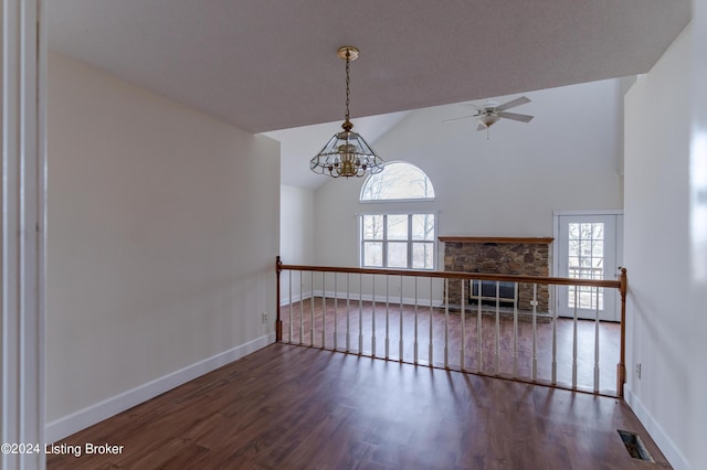 unfurnished living room featuring a fireplace, ceiling fan with notable chandelier, vaulted ceiling, and dark wood-type flooring