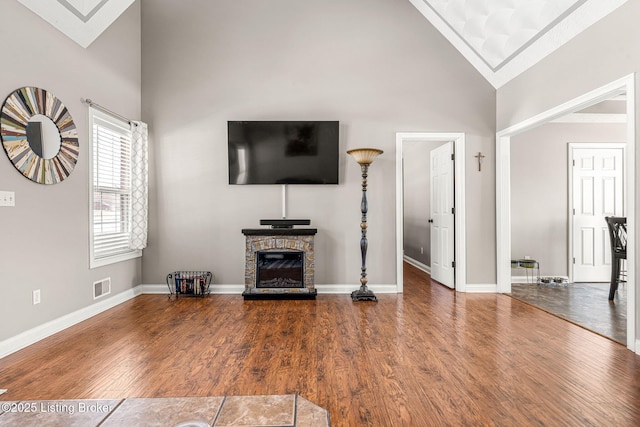 unfurnished living room featuring hardwood / wood-style flooring, a stone fireplace, and high vaulted ceiling