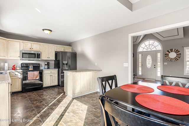 kitchen with appliances with stainless steel finishes, cream cabinetry, light stone counters, and a kitchen island