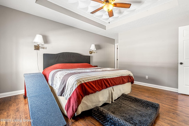 bedroom featuring ceiling fan, dark hardwood / wood-style floors, and a tray ceiling