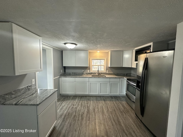 kitchen with light stone counters, a textured ceiling, stainless steel appliances, sink, and white cabinetry