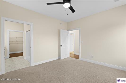 unfurnished bedroom with a walk in closet, ceiling fan, a closet, and light colored carpet