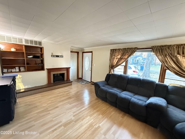 living room featuring crown molding, light hardwood / wood-style flooring, and a tiled fireplace