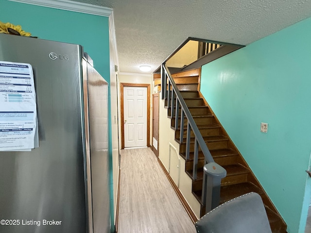 stairs with wood-type flooring, a textured ceiling, and ornamental molding