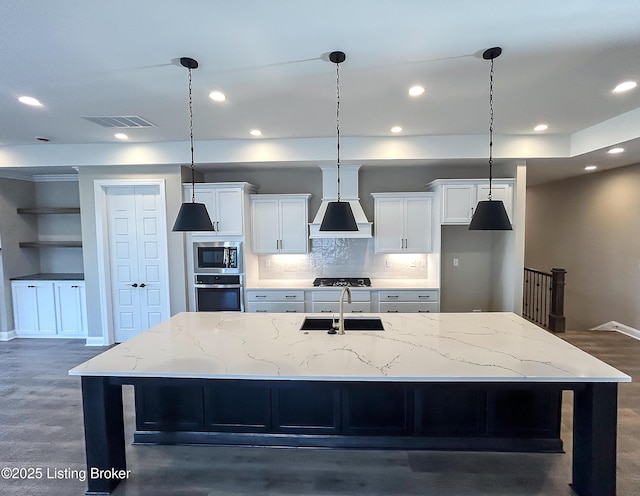 kitchen featuring premium range hood, a large island with sink, white cabinets, sink, and stainless steel appliances