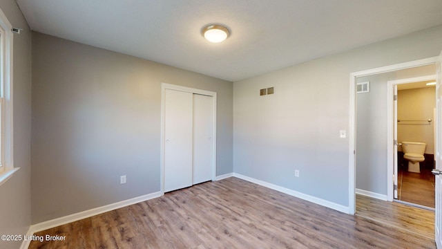 unfurnished bedroom featuring light hardwood / wood-style floors, a closet, and ensuite bath