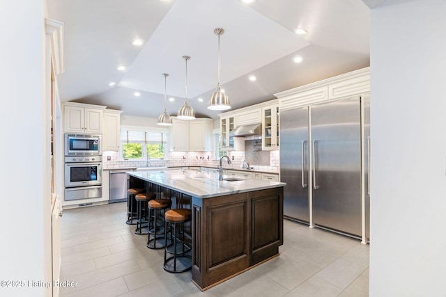 kitchen with a warming drawer, backsplash, vaulted ceiling, a sink, and built in appliances