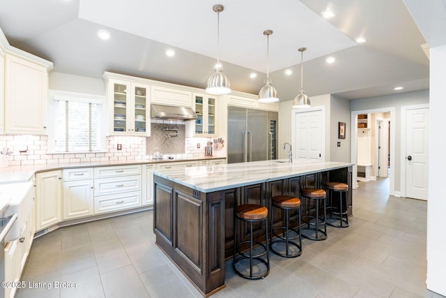 kitchen featuring built in fridge, a large island, vaulted ceiling, a kitchen breakfast bar, and exhaust hood