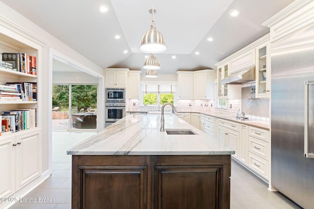 kitchen with lofted ceiling, glass insert cabinets, a sink, built in appliances, and under cabinet range hood