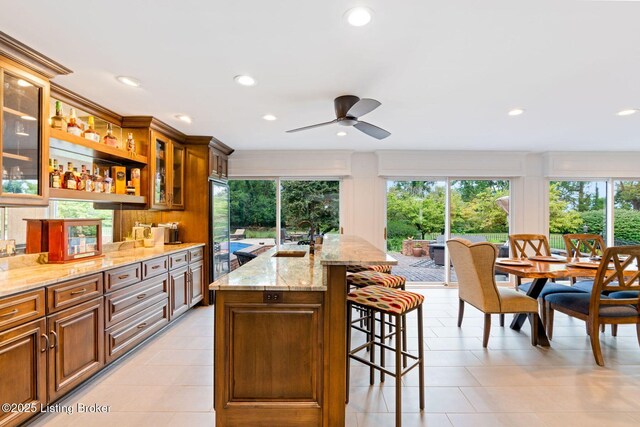 kitchen featuring a center island with sink, glass insert cabinets, a breakfast bar, light stone countertops, and a sink