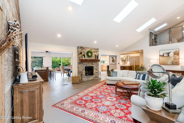 living area with high vaulted ceiling, a skylight, a stone fireplace, and recessed lighting