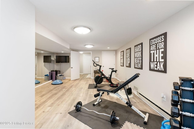 workout area with baseboards, baseboard heating, and wood finished floors