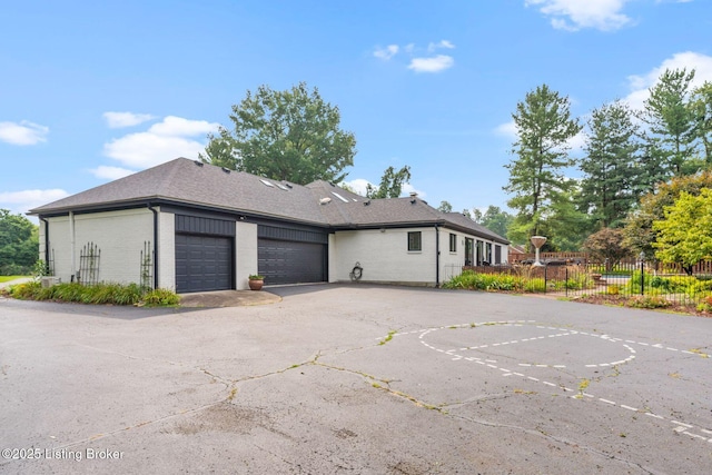 exterior space with brick siding, roof with shingles, fence, a garage, and driveway