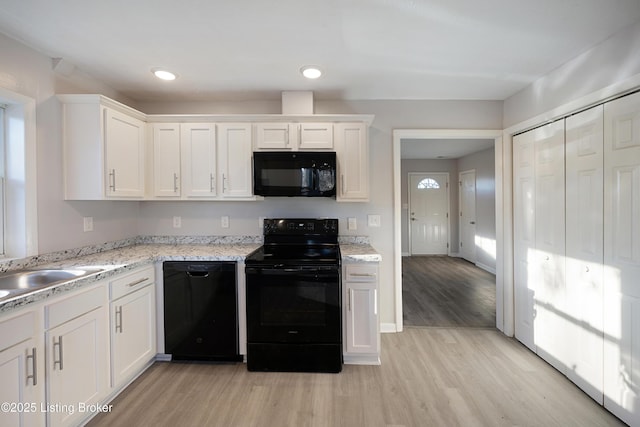 kitchen with light stone countertops, white cabinetry, sink, light hardwood / wood-style flooring, and black appliances