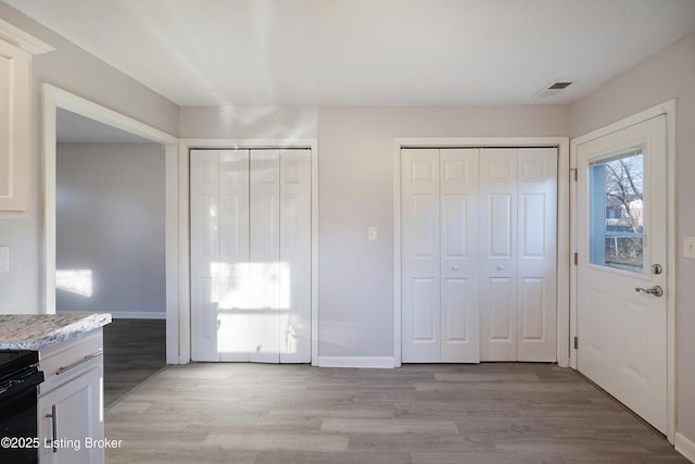 interior space featuring white cabinets, light hardwood / wood-style floors, stove, and light stone counters