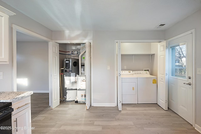 clothes washing area featuring washing machine and clothes dryer, water heater, and light wood-type flooring