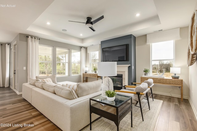 living room featuring a fireplace, wood-type flooring, a tray ceiling, and ceiling fan