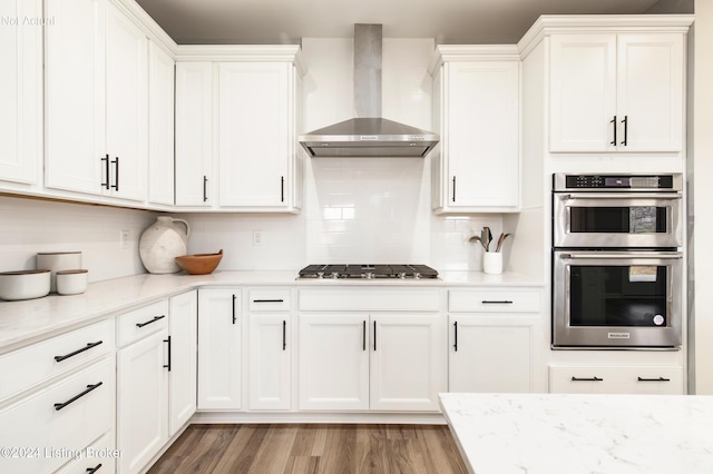 kitchen featuring white cabinets, appliances with stainless steel finishes, light stone counters, and wall chimney exhaust hood