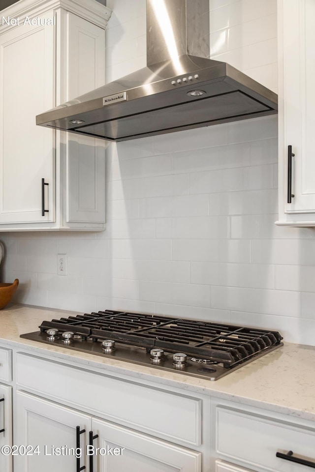 kitchen featuring decorative backsplash, light stone counters, wall chimney exhaust hood, stainless steel gas cooktop, and white cabinets