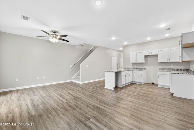 kitchen with white cabinetry, sink, ceiling fan, light stone counters, and light hardwood / wood-style floors