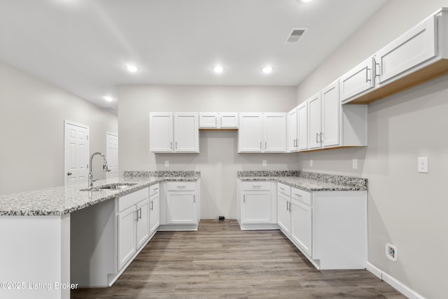 kitchen featuring white cabinets, sink, light wood-type flooring, light stone countertops, and kitchen peninsula