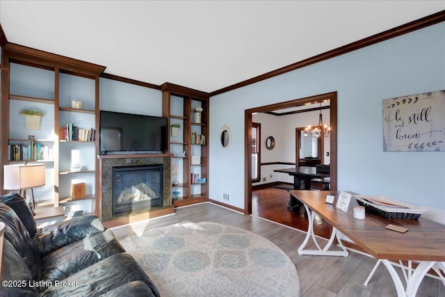 living room featuring wood-type flooring, crown molding, a high end fireplace, and an inviting chandelier