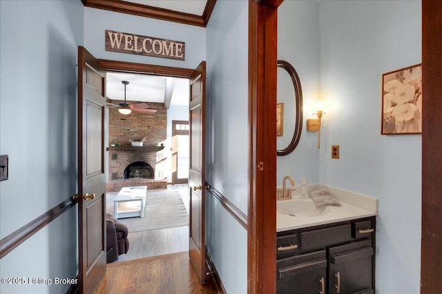 bathroom featuring hardwood / wood-style floors, vanity, crown molding, ceiling fan, and a fireplace