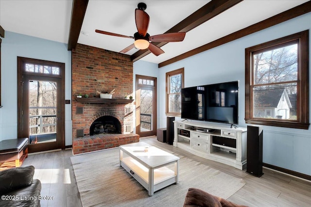 living room with a wealth of natural light, beamed ceiling, light hardwood / wood-style floors, and a brick fireplace