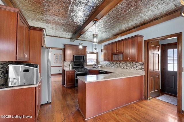 kitchen with wood-type flooring, sink, hanging light fixtures, appliances with stainless steel finishes, and kitchen peninsula