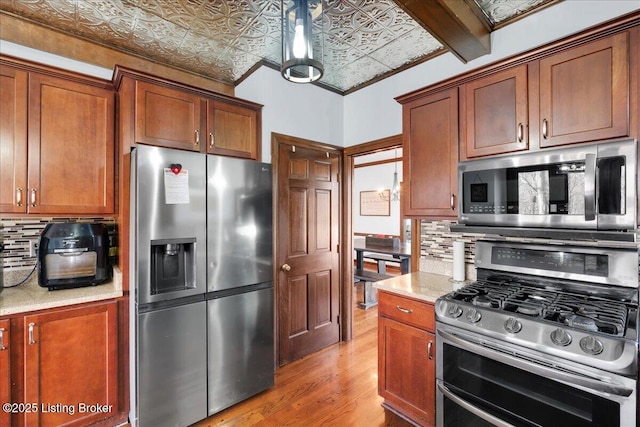 kitchen featuring beam ceiling, light stone countertops, light hardwood / wood-style floors, decorative backsplash, and appliances with stainless steel finishes