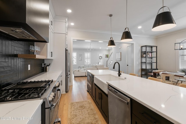 kitchen featuring wall chimney range hood, sink, light stone countertops, decorative light fixtures, and stainless steel appliances