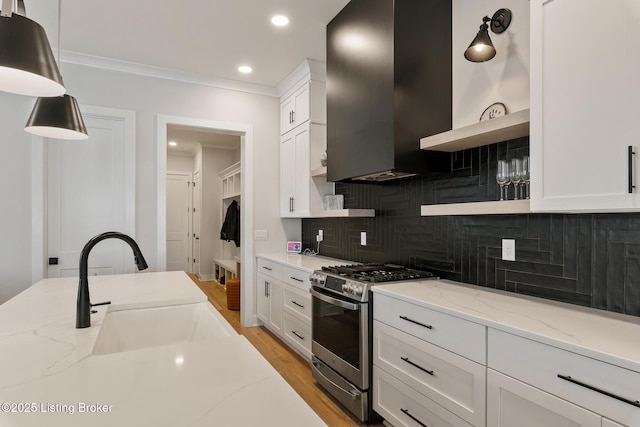 kitchen with stainless steel gas range oven, light stone counters, white cabinets, and wall chimney range hood